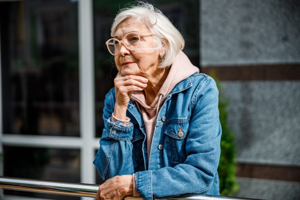 starija ženska osoba drži ruku pod bradom i zamišljeno gleda u daljinu